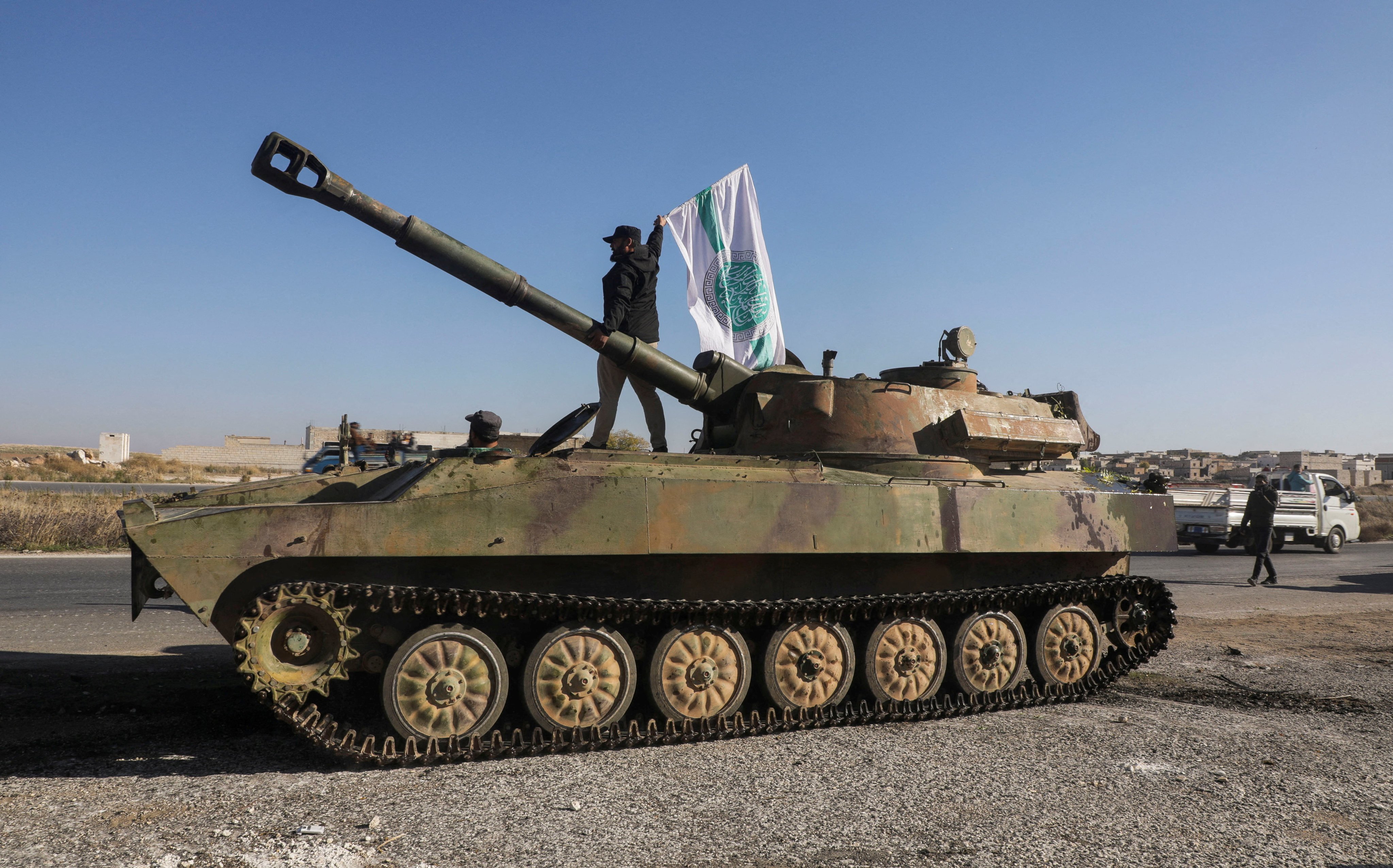 A rebel fighter stands atop of a military vehicle as he carries a Hayat Tahrir al-Sham flag in northwestern Idlib province, Syria on December 1. Photo: Reuters